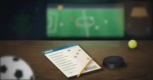 Pöydällä lyijykynällä täytetty vedonlyöntikuponki, jääkiekko, tennispallo ja jalkapallo, taustalla televisiossa näkyvä jalkapallo-ottelu.