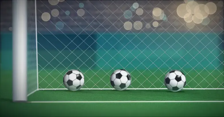 Kolme jalkapalloa lepää maaliverkossa maaliviivan takana valonheittimien valaisemalla stadionilla illalla.